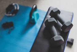 home gym and fit lifestyle still-life, room with flat bencha nd dummbells surrounded by other fitness equipment like yoga mat with kettlebell and jumping rope shot at shallow depth of field