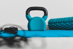 home gym and fitness routines concept, blue yoga mat with kettlebell foam roller and jumpying rope shot at shallow depth of field from low perspective