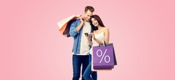 Holiday sales actions, rebates, discounts offers concept image - happy couple with shopping bags, looking at mobile smart phone, isolated over pink color background. % sign. Valentines Day holiday.