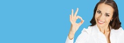 Businesswoman in white confident clothing showing ok hand sign gesture, isolated on blue background. Portrait of happy smiling gesturing brunette woman at studio. Business concept.