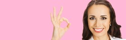 Businesswoman in white confident clothing showing ok hand sign gesture, rose pink color background. Portrait of happy smiling gesturing brunette woman at studio. Business concept photo.