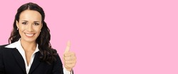 Businesswoman in black confident suit showing thumbs up gesture, over rose pink color background. Happy smiling gesturing brunette woman at studio. Business concept photo.