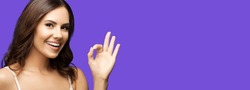 Photo of woman making ok okay hand sign or zero gesture, isolated on violet purple color background. Happy smiling gesturing brunette girl at studio. Wide horizontal banner composition.