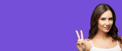 Photo of woman showing two fingers or victory hand sign gesture, isolated on violet purple background. Portrait of happy smiling gesturing brunette girl at studio. Wide horizontal banner composition