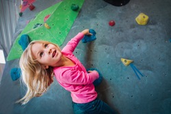 Cute girl climbing on artificial boulders wall in gym