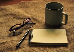 Top view of writer objects concept: notebook, pen, eyes glasses and cup of coffee on sack cloth in retro filter effect