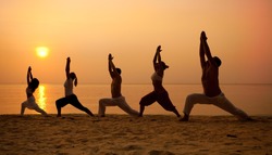 Five people practising yoga at the beach - warrior I pose.