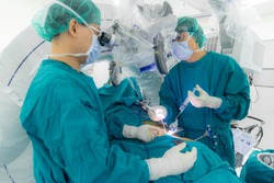 Asian doctor working inside the modern operating room and perform surgery with microscope assistance.Surgeon in green surgical gown suit. Medical concept.