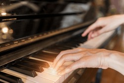 Hands of woman playing grand piano in musical school.Two hand with different level and keyboard.Blur background with light.Female pianist hands on grand piano keyboard.Playing music or song at home.