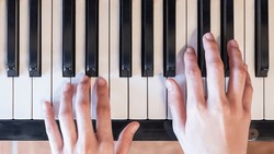 Hands of woman playing grand piano in musical school.Two hand with different level and keyboard.Blur background.Female pianist hands on grand piano keyboard.Playing music or song at home.Top view.