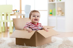 Smiling baby boy sitting inside cardboard box after moving to a new apartment