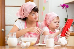 Mother and child preparing pastry together at kitchen and looking at cookbook