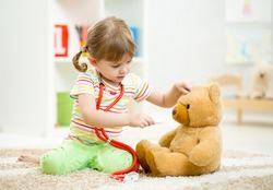 child girl playing doctor and curing plush toy indoors