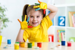Funny child girl with hands painted in colorful paint at home