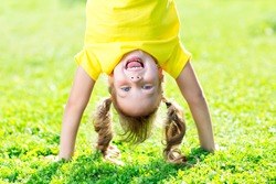 Portraits of happy kid playing upside down outdoors in summertime standing on hands on grass