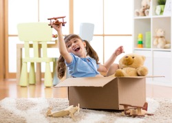 Kid girl playing pilot flying a cardboard box in children room