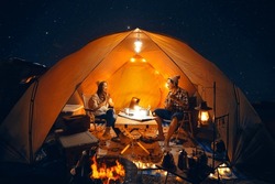 Asian couple enjoy in they tent in camping trip on night time with many star on the sky, they enjoy coffee, music, singing and sweet in camp