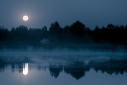 Night mystical scenery. Full moon over the foggy river and its reflection in the still water.