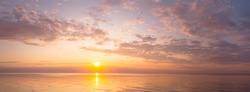 Wide panorama of beautiful warm sunset over calm sea and sky with clouds.