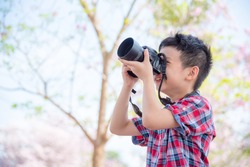 Young asian boy taking photo by camera in park