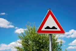 Red European warning traffic sign triangle uneven surface in front of cloudy sky in summer