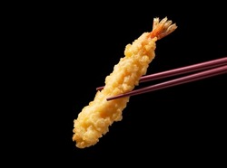 Shrimp tempura lifted with chopsticks against a black background. Tempura is a Japanese food. This is Japanese fried shrimp.