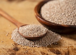 White chia seeds and wooden spoon in a wooden dish placed on a wooden background. Close-up. 