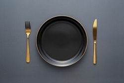 Gold knives and forks on a black background, empty black plate. Beautiful gold cutlery. View from above.