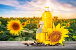 Bottles of sunflower oil with seeds and flower on a wooden table against the background of a field with sunflowers