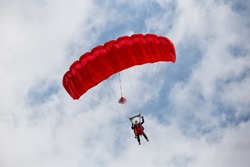 Parachuter descending with a red parachute against blue sky