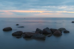 Blue hour after the sunset over rocky Baltic sea cost. Small stones and big boulders in the sea. Long exposure photo.
