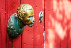 The small metallic head of human, as handle on the red door.