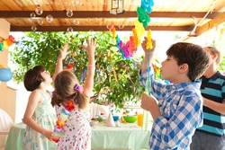 Group of children having fun at a birthday party in a home garden blowing and catching bubbles joyfully, house exterior. Kids playing at party, outdoors. Fun and activities on holiday, sunny day.