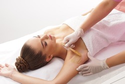 Beautician is removing hair from young female armpits with hot wax. Woman has a beauty treament procedure. Depilation, epilation, skin and health care concepts.