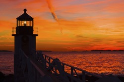 Marshall Point Lighthouse with orange sky at sunset on the coast of Maine.