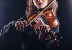 Beautiful young woman playing the violin on dark background