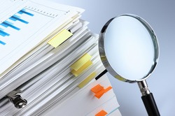 Investigate and analyze. Scanning business documents. Magnifying glass and stack of documents. 