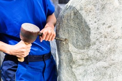 Stonemason working on boulder with sledgehammer and iron in workshop
