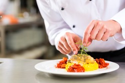 Chef in hotel or restaurant kitchen cooking, he is finishing a dish on plate