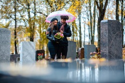 Couple mourning a deceased loved one on cemetery in fall standing between the graves