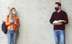 Two students standing in social distance wearing face mask looking at each other