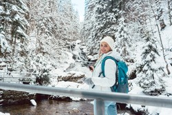 Hiker woman in front of small waterfall in the woods during winter