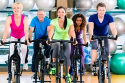 Fitness group of men and women spinning of bike in gym to gain strength and fitness