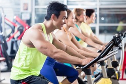 Group of young Asian athletes side by side during spinning class workout