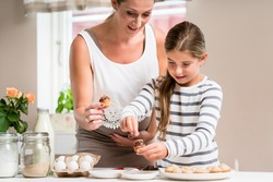 Pregnant mum and her little daughter baking together and decorating the cupcakes