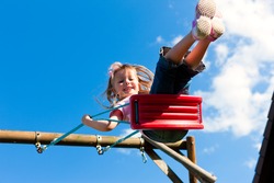 Little girl child sitting on a swing in the garden playground; she has lots of fun