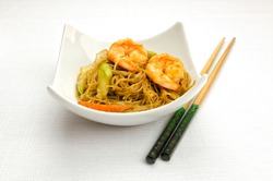 Chinese food, fried rice noodles with shrimps and vegetables served in a bowl with chopsticks