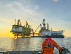 Oil and gas industry. Marine crew standing on supply vessel looking oil and gas platform during sunrise.