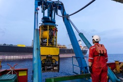 A techinician standing nearby Remoted Operated Vehicle (ROV) hanging on Launch & Recovery System (LARS) for underwater pipeline survey and inspection nearby Floating Storage Offloading (FSO) vessel.