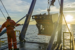 worker recovering robotics Remote Operated Vehicle (ROV) after entering sea surface during oil and gas pipeline inspection in the middle of South China Sea isolated on sunrise with glare
